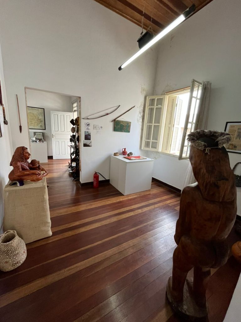 Sala com esculturas, janelas abertas e piso de madeira