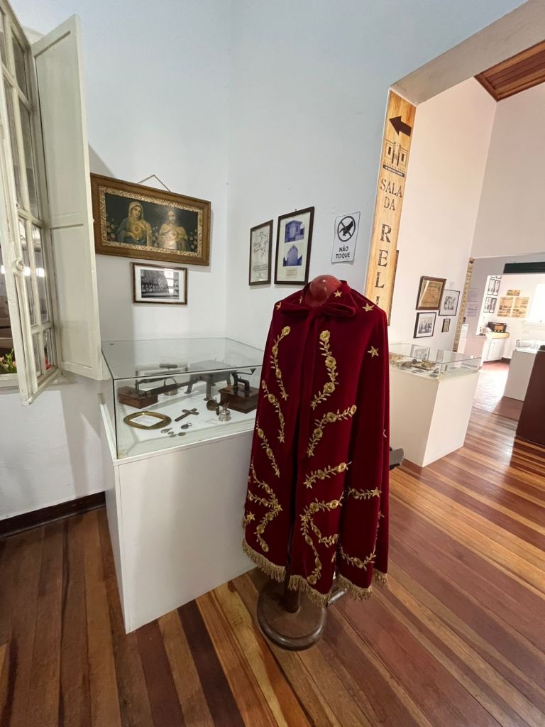 Traje religioso vermelho e vitrines em sala expositiva